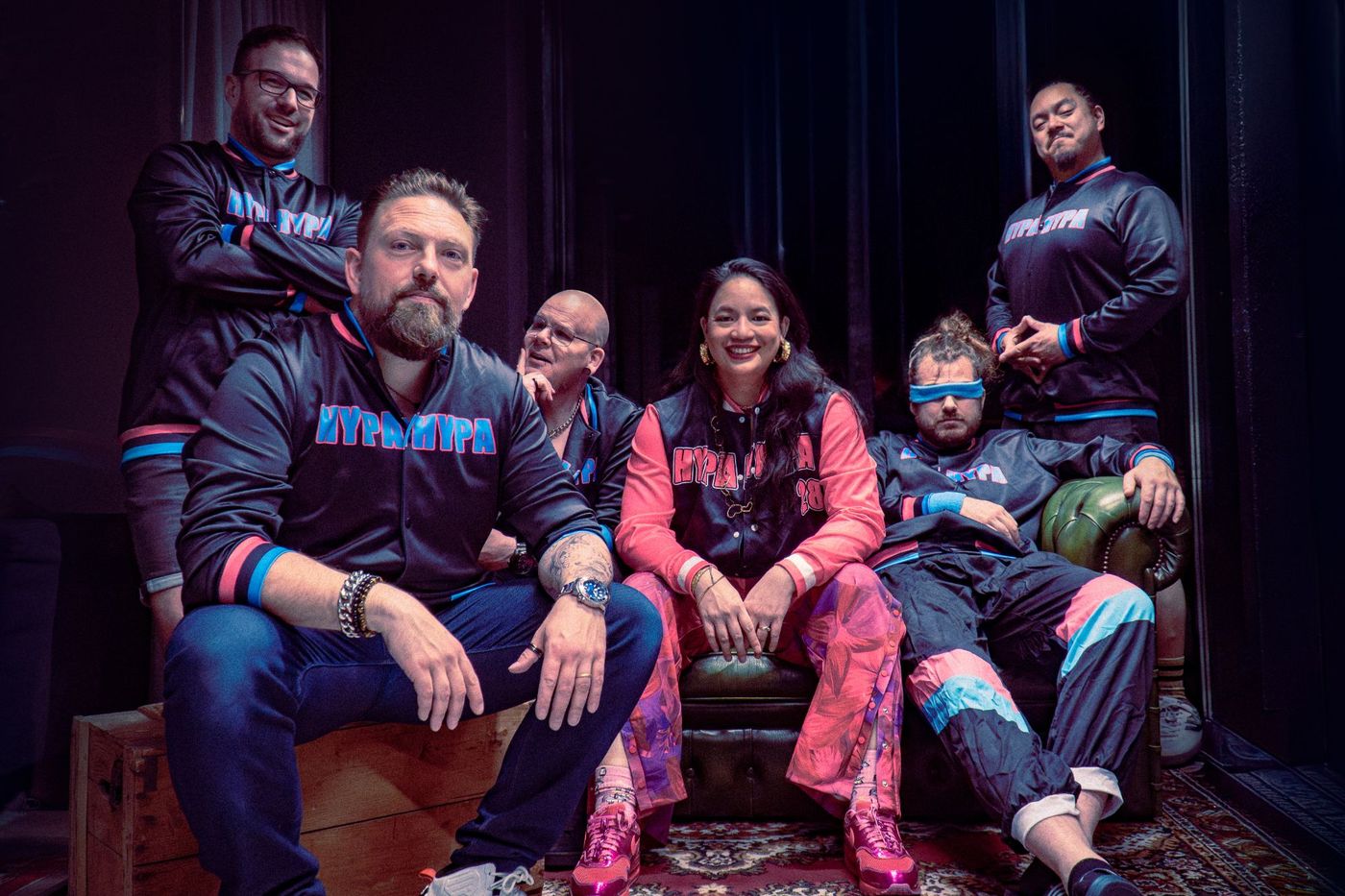 HypaHypa in bijpassende HypaHypa-jacks rond een groene chesterfield, één bandlid met een blauwe zweetband over de ogen